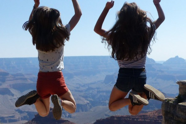 Duas meninas pulando de felicidade, ambas de costas.